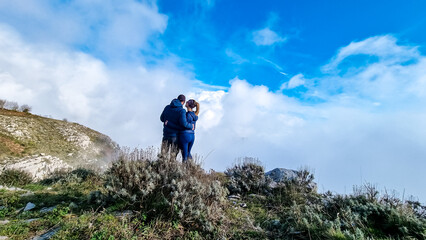 Couple with scenic view from Monte Comune on thick white clouds and blue sky near coastal town...