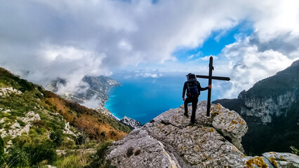 Active man at summit cross near Santa Maria del Castello. Scenic view on coastal town Positano,...