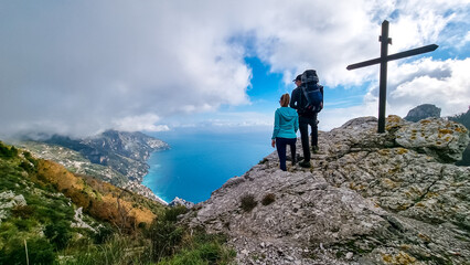 Active couple at summit cross near Santa Maria del Castello. Scenic view on coastal town Positano, Praiano. Magical hiking trail, Lattari Mountains, Apennines, Amalfi Coast, Campania, Italy, Europe
