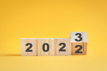 Wooden cube stock flipping, change from 2022 to 2023. Yellow color background, with copy space. - obrazy, fototapety, plakaty