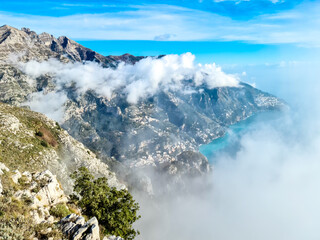 Panoramic view from Monte Comune on the coastal town Positano appearing from clouds. Magical hiking above thick fog in Lattari Mountains, Apennines, Amalfi Coast, Campania, Italy, Europe. Misty vibes