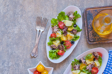 Potato salad with octopus, tomato and leaf lettuce on a gray oval plate on a gray concrete background. Mediterranean, Italian cuisine.