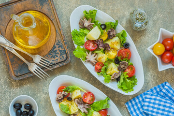 Potato salad with octopus, tomato and leaf lettuce on a gray oval plate on a gray concrete background. Mediterranean, Italian cuisine.