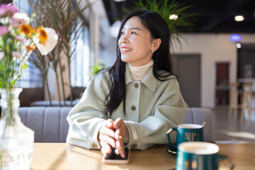 Candid lifestyle portrait of Beautiful young millennial asian girl drinking coffee in modern cafe and smiling