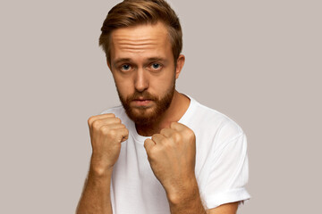 Image of young hipster guy in white, having sad blue eyes keeping fists in protective boxing...