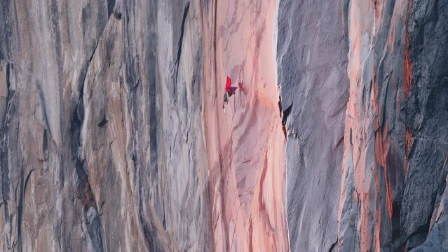 Yosemite Firefall at Sunset 6K RED camera Shot, Yosemite National Park, California. Mountain climber hanging on rope on El Capitan mountain in cinematic red orange light at sunset. Extreme sport shot