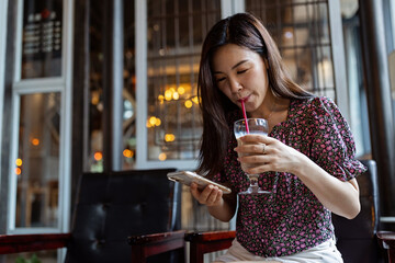 Smiling Asian Woman Talking On Cellphone In Cafe, Managing Her Business Schedule, Planning Meetings, Talking With Client or friends, Sitting At Table In modern Cafeteria