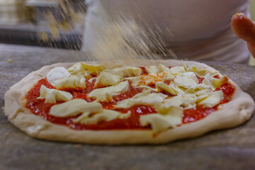 Pizzaiolo napoletano mentre mette del formaggio su una pizza margherita napoletana condita con...