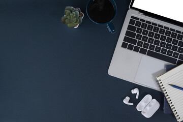 Computer laptop, cup of coffee, notebook and wireless earphone on dark blue background. Flat lay. - obrazy, fototapety, plakaty