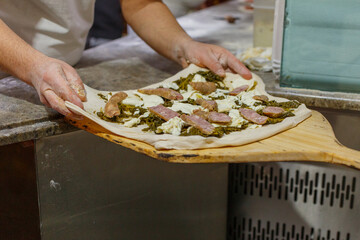 Pizzaiolo napoletano mentre stende su una pala di legno da forno di una pizzeria una pizza con...