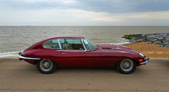 Classic  Red E type Jaguar parked on seafront promenade beach and sea in background