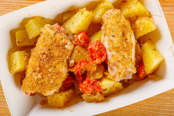 Vaschetta di cartone per alimenti con patate al forno, pomodori e involtini di pesce impanati preparata per un pranzo da asporto