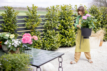 Young woman taking care of flowers in the garden. Cheerful florist or housewife replanting hydrangeas on table outdoors. Concept of gardening and floristics