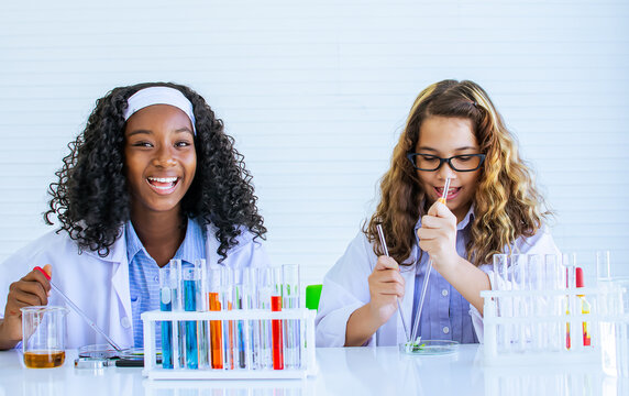 African black and caucasian girls studying science and making experiment with fun, happiness in laboratory at school. Education and Diversity Concept.