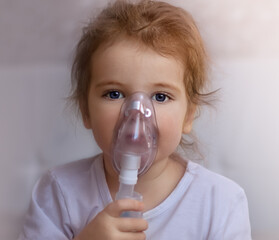 a little girl in a white t-shirt sits on the bed and breathes with an inhaler. concept of medicine, health.