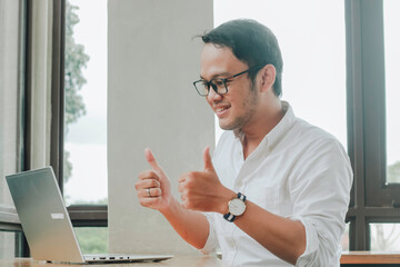 Young Asian man doing video conference on laptop computer while sitting at the cafe, having meeting