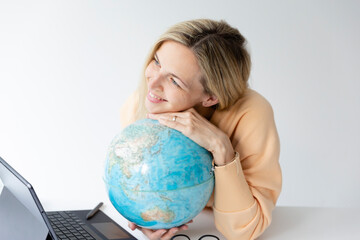 pretty young woman standing at height adjustable table plans her vacation with globe in hand and notebook and is daydreaming