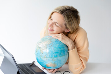 pretty young woman standing at height adjustable table plans her vacation with globe in hand and...