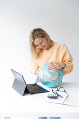 pretty young woman standing at height adjustable table plans her vacation with globe in hand and notebook and is daydreaming