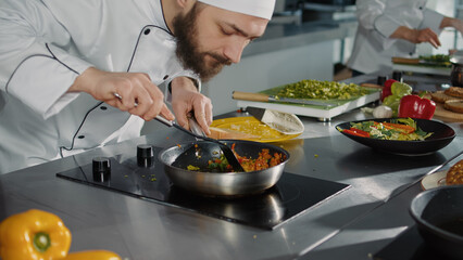 Professional cook preparing culinary recipe with vegetables, using frying pan on stove to make fresh gourmet meal. Male chef cooking gastronomic dish in authentic kitchen. Close up.