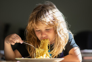 Close up portrait of funny kid eating noodles pasta spaghetti. Little boy having breakfast in the...