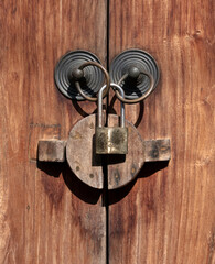 Close up of old brass ring door handles with padlock against wood door texture