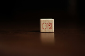 Oops sign on wooden cube over yellow background.