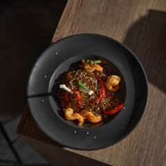 Funchoza with shrimp and vegetables on the table, copy space. Buckwheat noodles on a dark stone background. Asian cuisine, Wok menu. Traditional Asian food