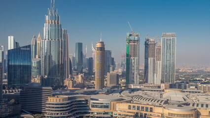 Naklejka na ściany i meble Skyscrapers rising above Dubai downtown timelapse, mall and fountain surrounded by modern buildings aerial top view