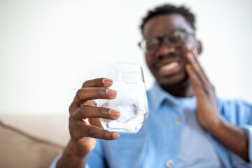 Young man with sensitive teeth and hand holding glass of cold water with ice. Healthcare concept....