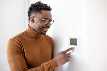 Smiling African American man using modern smart home system, controller on wall, positive young man...