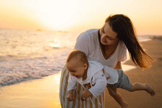 happy mother's day. Beautiful mother and baby play on the beach. Mum and her Child together enjoying sunset. Loving single mother hugs cute little son.