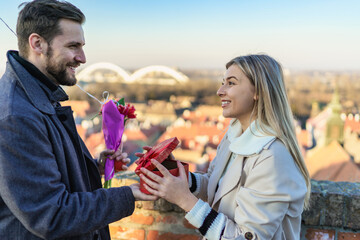 Happy couple with a gift, flowers and a balloon. The woman is surprised and overjoyed because of the beautiful gift she received from her man.