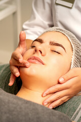 Fototapeta na wymiar Face massage. Beautiful caucasian young white woman having a facial massage with closed eyes in a spa salon