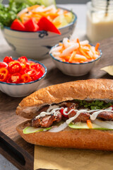 Banh Mi - Vietnamese sandwich with sausage, pork, lettuce, tomato and arugula on the light grey texture background. One of the most famous street food in the world