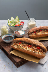 Banh Mi - Vietnamese sandwich with sausage, pork, lettuce, tomato and arugula on the light grey texture background. One of the most famous street food in the world