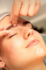 Fototapeta na wymiar Eyebrow massage. Beautiful caucasian young white woman receiving an eye and eyebrow massage with closed eyes in a spa salon