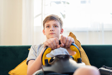 Teen boy gamer playing racing games on the computer. He uses the steering wheel. Getting ready for professional driving. Stimulation driving, child playing video game