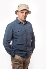 Portrait of a bearded middle-aged man in khaki trousers and hat looking thoughtfully at the camera over a white studio background with copy space