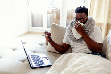 Sick young man blowing his nose talking to a doctor. Sick male complaining during video call with...