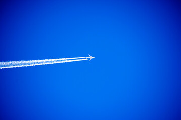 White plane high in the blue sky with a white trail. Transportation backgrounds