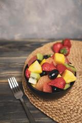 Fresh fruit salad, top view in a bowl on wooden background, vegetarian food concept