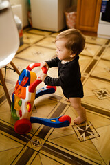 Cute baby boy with toy walker at home interior