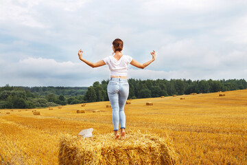 Naklejka na ściany i meble girl with straw hat stands on a haystack on a bale in the agricultural field after harvesting