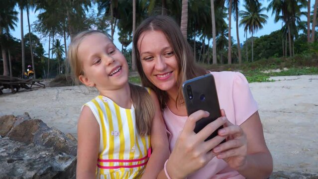 Mother take selfie picture and daughter kiss. Palm tree natural backround. Friendship, love and happy family forever on summer vacation. Child smile