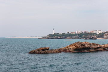 Unique rocky coastal formations repeating shape of sea waves, with lighthouse in background. Biarritz, French Basque Country