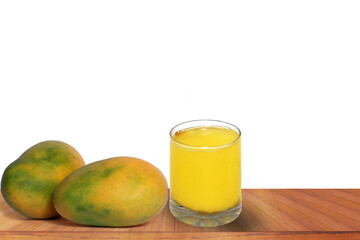 Mango juice in a glass and mangoes on a wooden table on a white background.