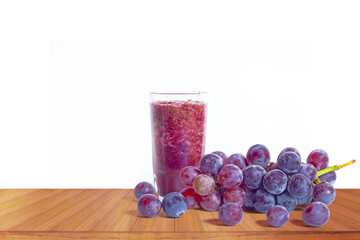 A glass of red grape juice and grapes on a wooden table on a white background