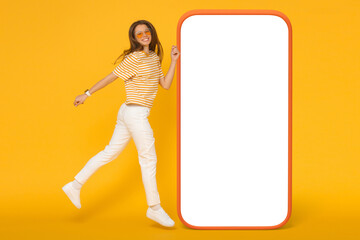 Carefree young woman in sunglasses jumping in the air into big screen of huge phone mockup