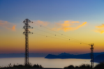 High voltage towers on coast at sunset